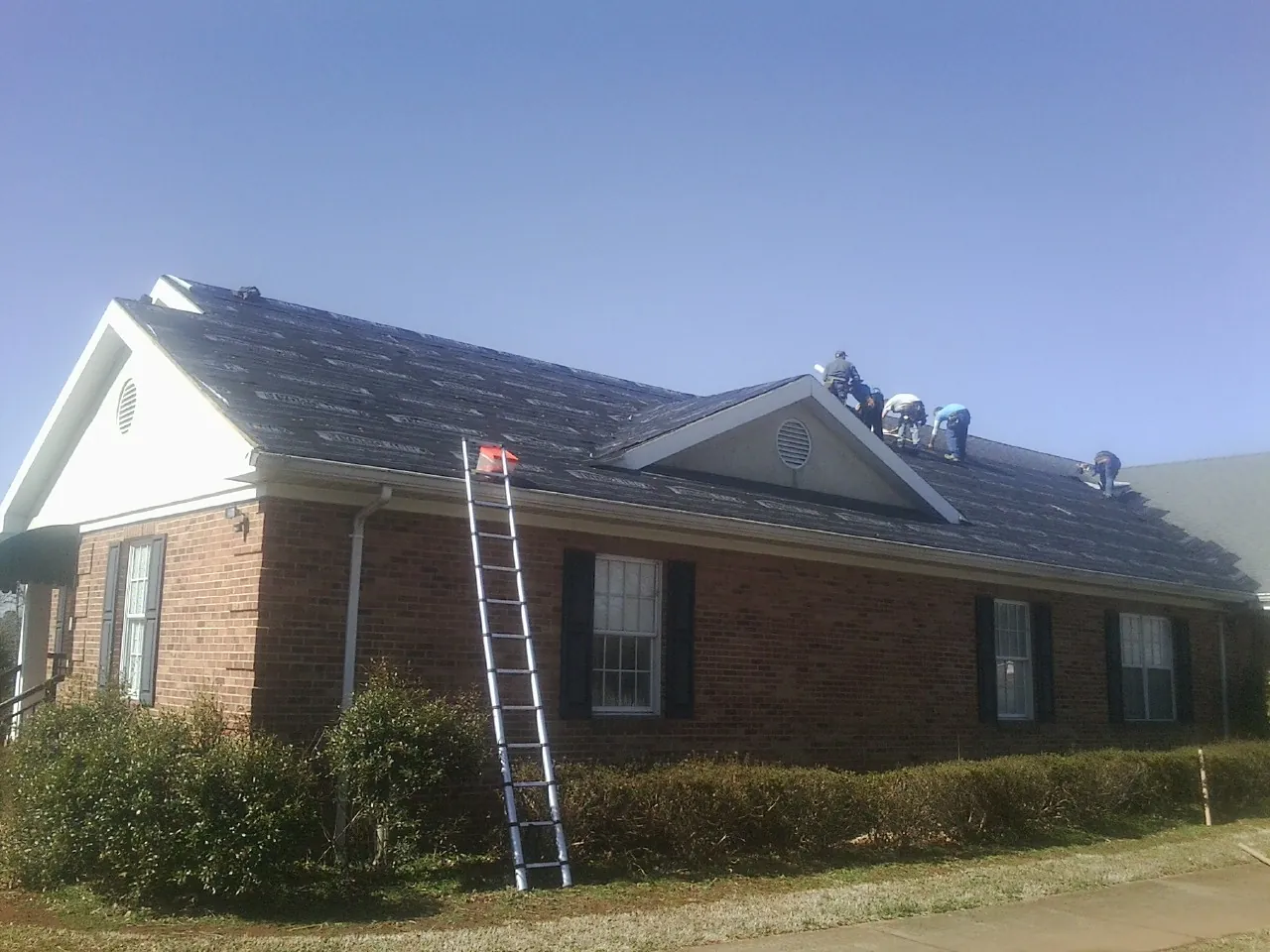 Crew tearing shingles off a brick ranch roof with a ladder set — Emergency Roof Repair work by our crew in Winchester
