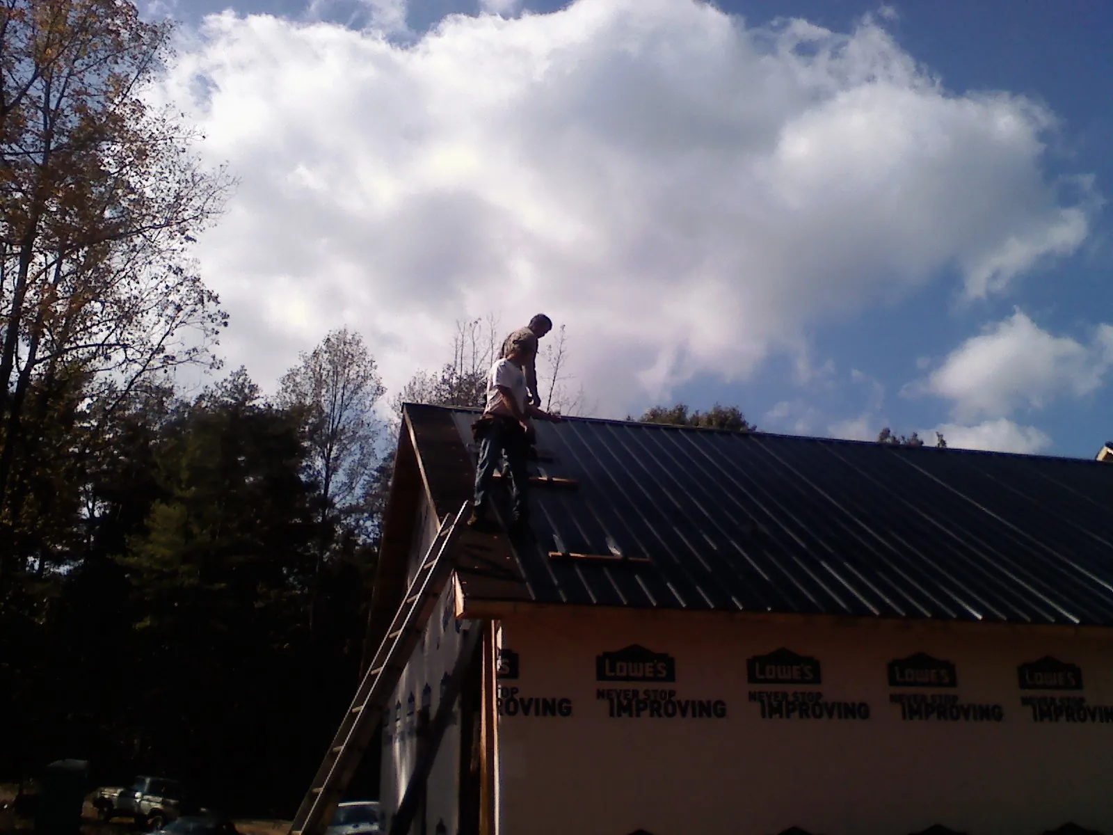 Roofer fastening dark metal panels high against a cloudy sky, from a Roof Inspection job in Winchester